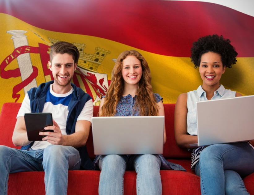 Young adults using electronic devices on couch  against digitally generated spanish national flag